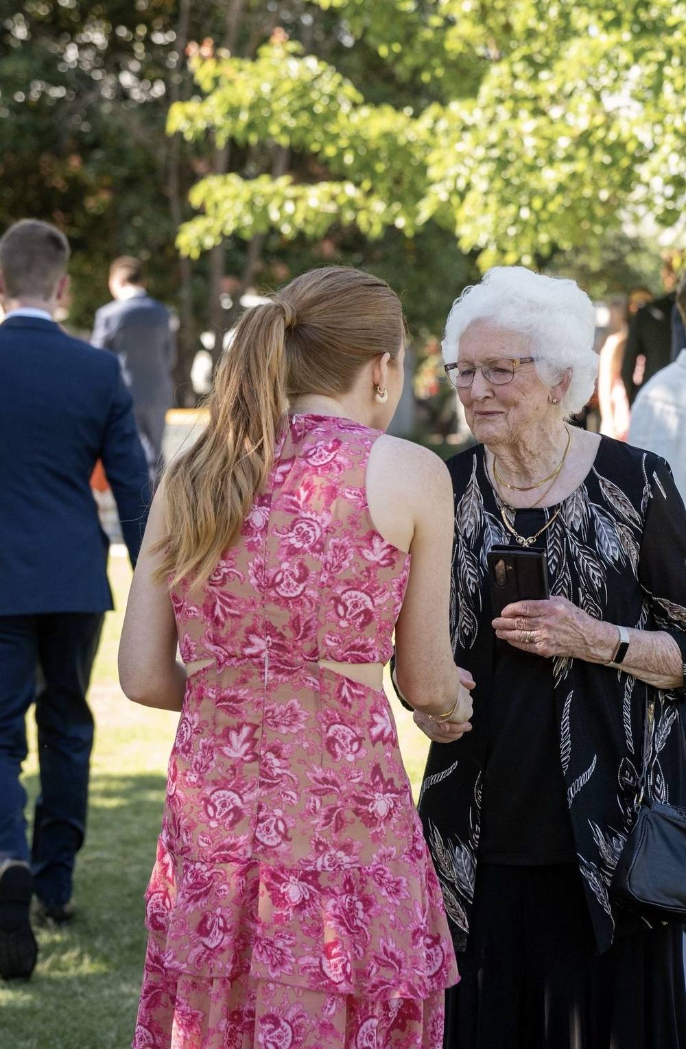 Katie holding hands with a smiling elderly guest on the lawn after a ceremony