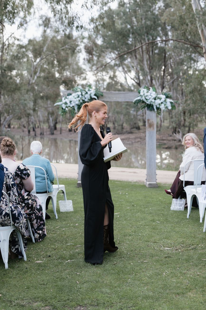 Katie laughing with a microphone in the aisle as smiling guests turn to watch